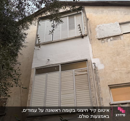 חזית בניין עם תריסים סגורים ועץ בחזית